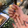 Rainbow Fairy Brown press-on nails worn on hands with brown-mauve tones, colorful gems and bow charms