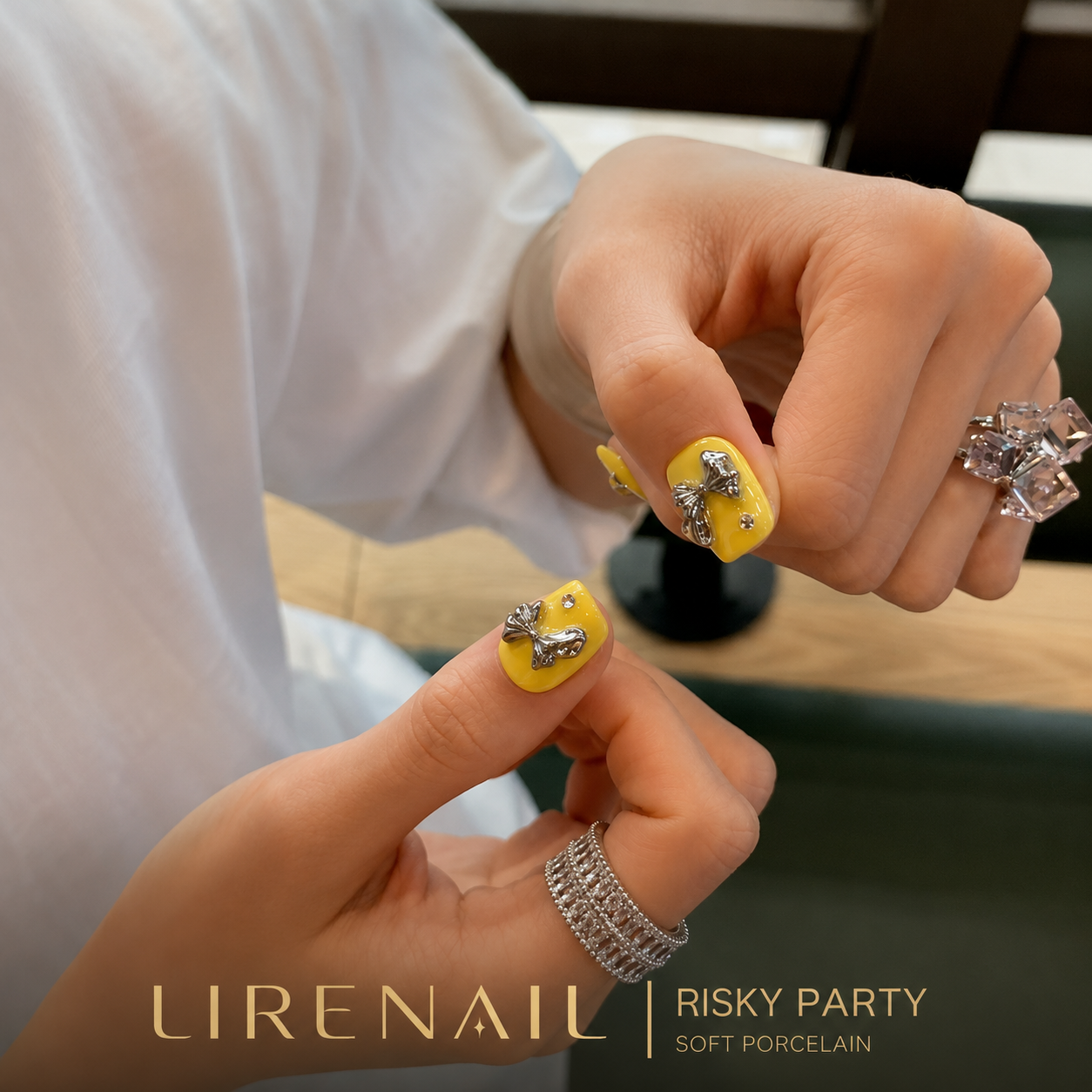 Close-up of Risky Party yellow press-on nails showing silver 3D bow detail on thumb